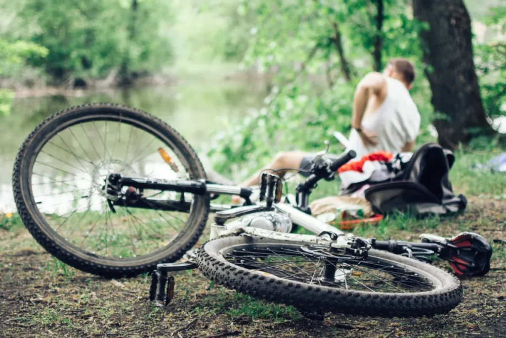 Bicycle lying in the grass by a lake path while the rider sits nearby
