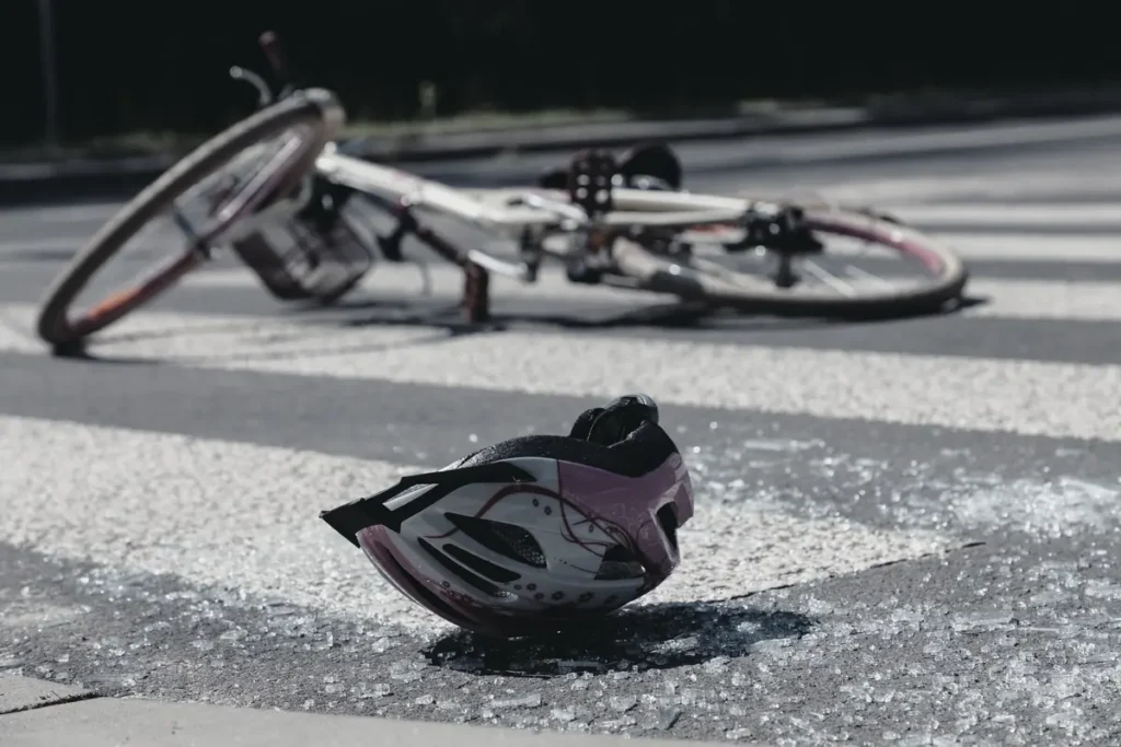Cracked bike helmet on the road next to a damaged bicycle