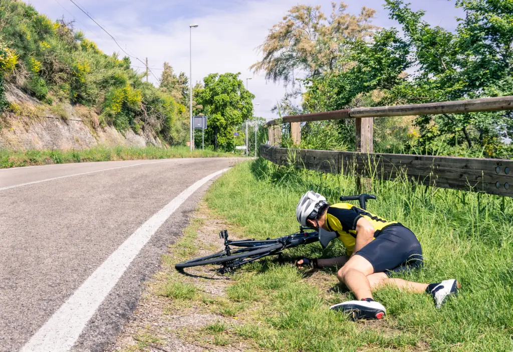 Cyclist lies in the grass beside a road after a crash
