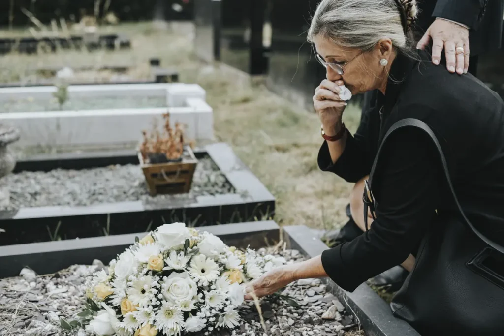 Woman mourns at a graveside with flowers