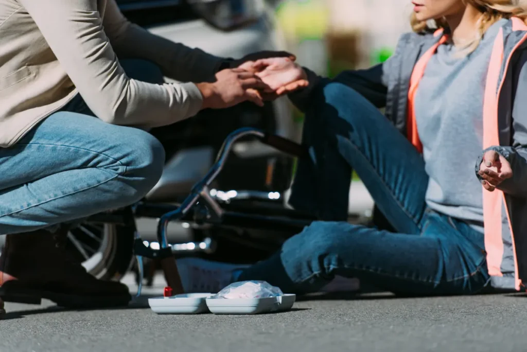 Man helps a woman who fell from her bike next to a car