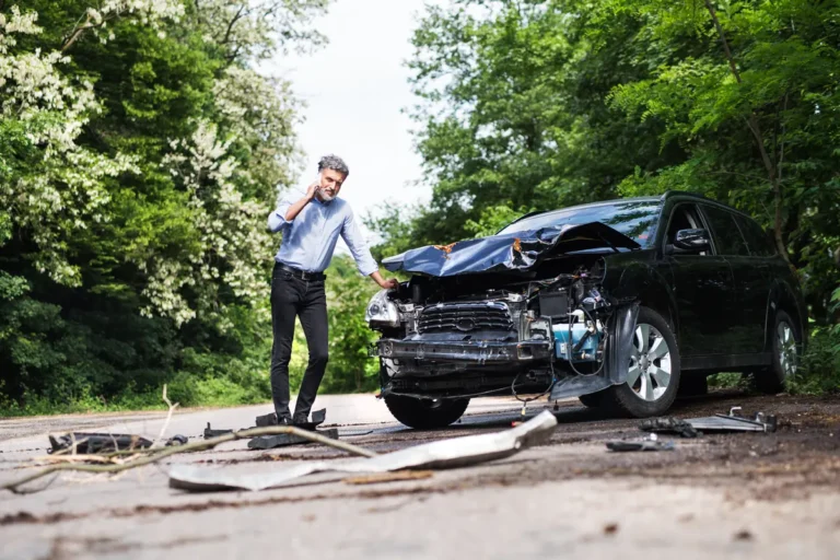 Man makes a phone call next to his damaged SUV after a crash