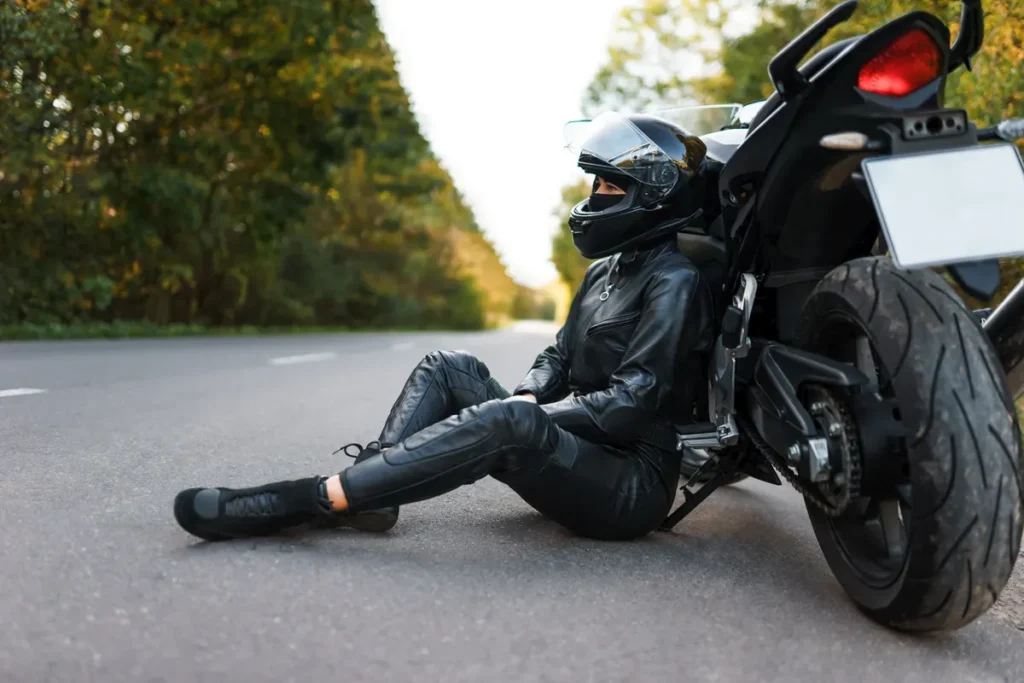 Motorcyclist in leathers sits on the road next to her motorcycle