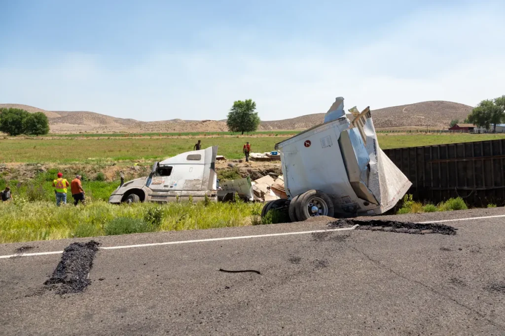 Semi-truck lying on its side next to a rural highway