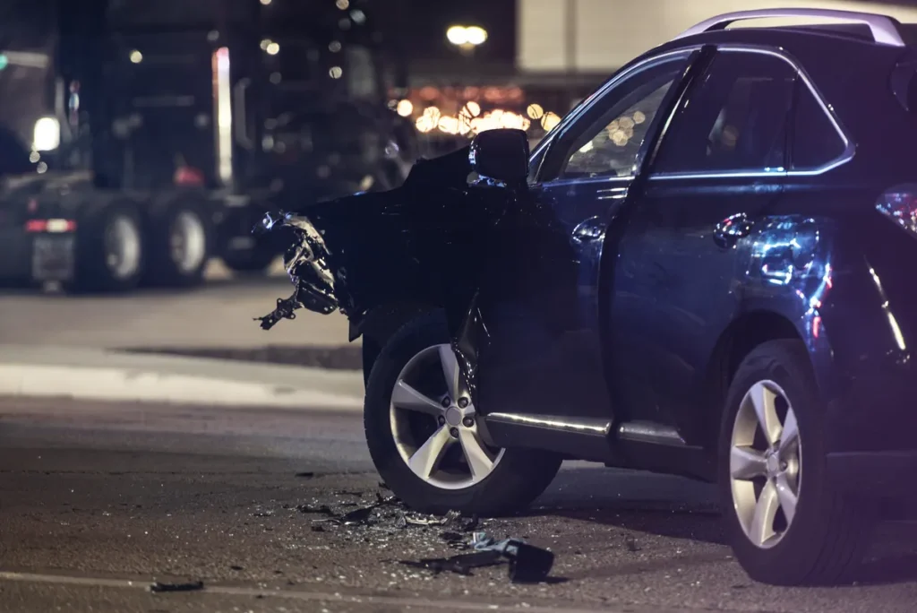SUV with a smashed front end on a city street at night