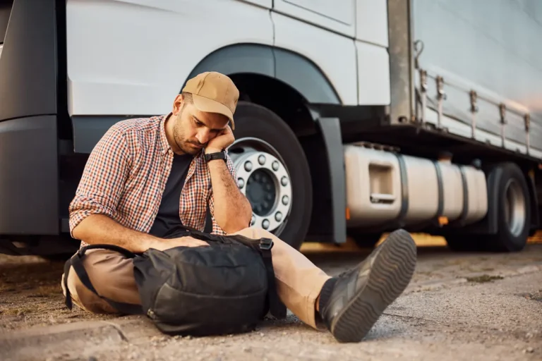 Tired truck driver resting on the ground beside his truck