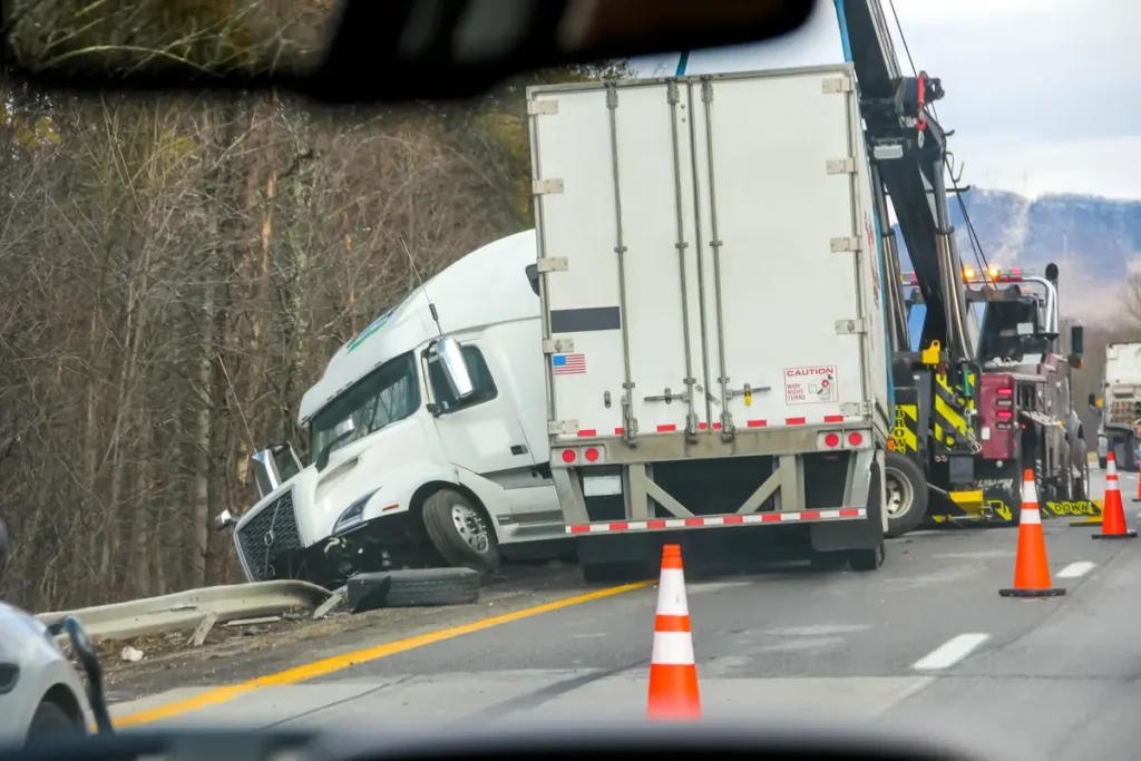 Box truck tipped on its side on a highway, with traffic cones