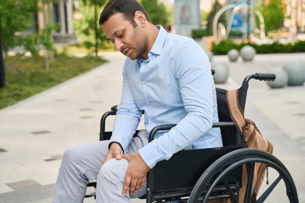 Man in a wheelchair rubbing his leg outdoors
