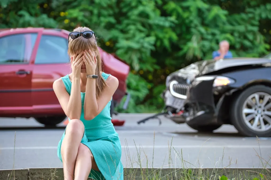 Upset woman sits by the road after a car crash