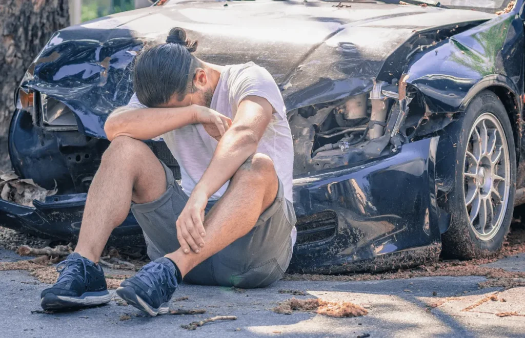 Shaken driver sits on the road beside a damaged car